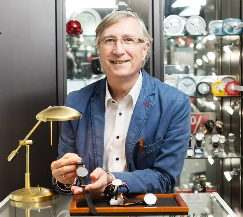 Juwelier Jörg Plüschau steht in seinem Geschäft und präsentiert der Kamera eine hochwertige Armbanduhr.